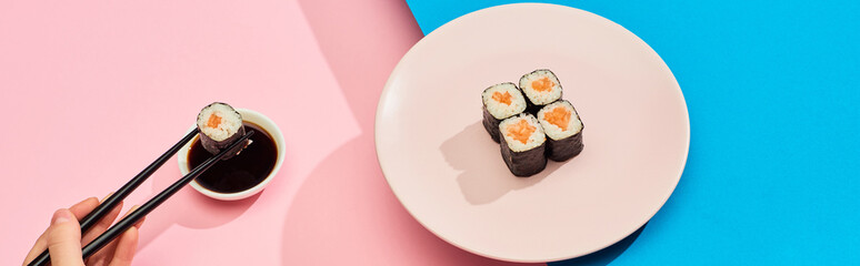 cropped view of woman eating fresh maki with salmon near soy sauce on blue, pink background, panoramic shot © LIGHTFIELD STUDIOS