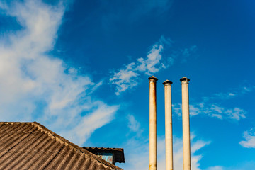 Roof of a residential building and chimney against a cloudy blue sky.
