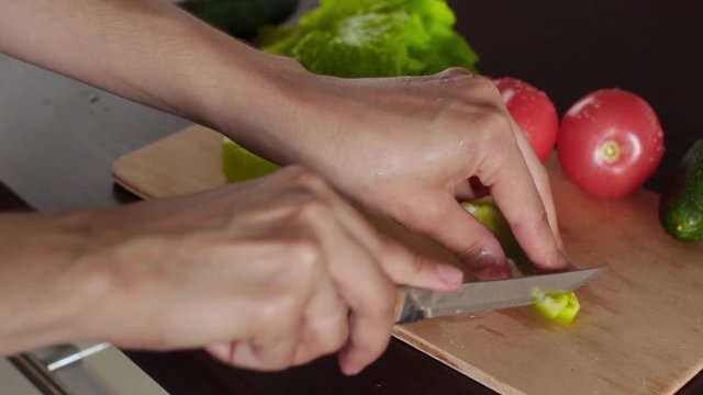 young woman making green salad with cucumber, tomatoes, green pepper, lettuce in a kitchen