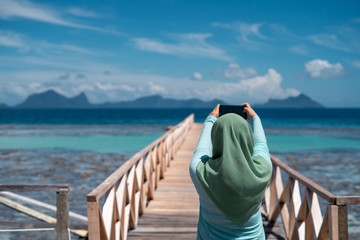 Vacation and technology. Outdoor portrait of  woman in hijab taking photo of the scenery with her...