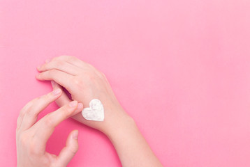 Hands of a beautiful well-groomed woman with a cream jar on a pink textural background. Moisturizer for clean and soft skin in the winter. The heart shape is made of cream. I love the body. 