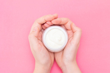 Hands of a beautiful well-groomed woman with a cream jar on a pink textural background. Moisturizer for clean and soft skin in the winter. I love the body. Healthcare concept.