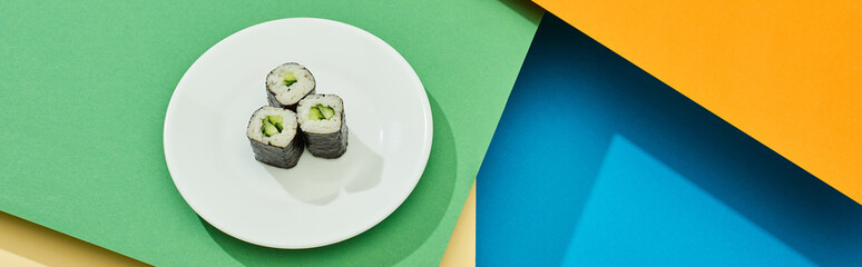 fresh maki with cucumber on plate on multicolored surface, panoramic shot