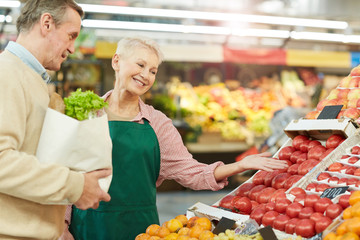 Waist up portrait of smiling senior woman selling fruits and vegetables to customer while working at market, copy space