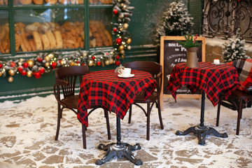 Empty terrace of cafe and restaurant with tables and chairs decorated for Christmas. Stylish Christmas decorations garlands and fir branches on windows of cafe on European city street. festive decor 