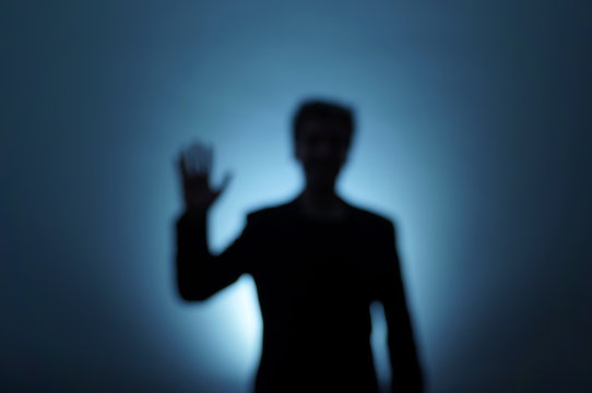 Unfocused backlit man moves his hand to say hello. Near-death experience. Dream image.