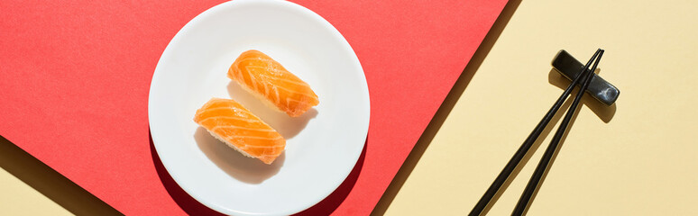 top view of fresh nigiri with salmon near chopsticks on red and beige surface, panoramic shot