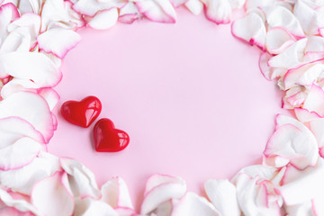 Two little red hearts and white with pink rose petals forming round shaped frame on pink pastel background. Valentines, Wedding, Women's Day greeting card with copy space for you text. Selective focus