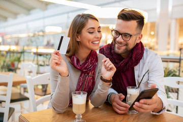 A couple is testing out a new debit card by buying something they like over the phone. They are making a choice at the moment. She might have found what she likes. Cafe inteiror.