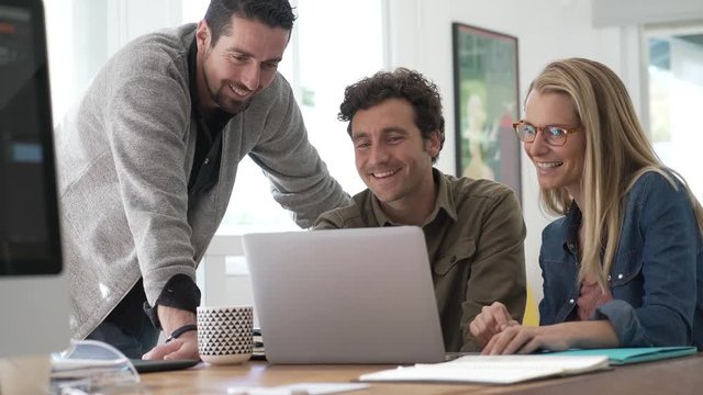 Co-workers gathering in office and using laptop