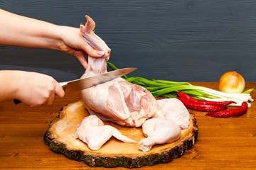 Cook chef hands woman cuts carcass of whole chicken on a wooden background.