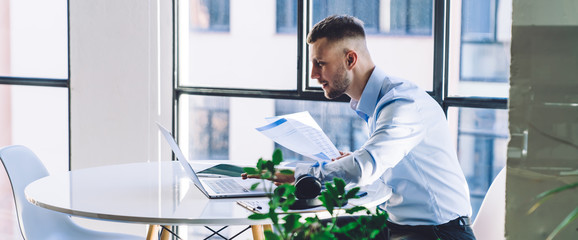 Interested businessman reviewing report and surfing laptop at work