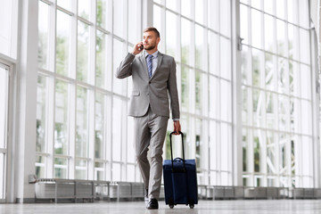 business trip, corporate and people concept - young businessman walking with travel bag along...