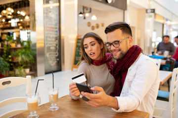 A husband and wife typing on the phone the bank card details to finalize a purchase.