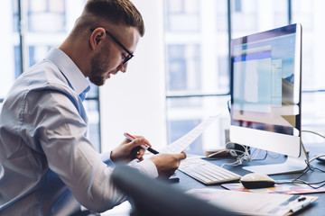 Serious manager checking document with pen at working table