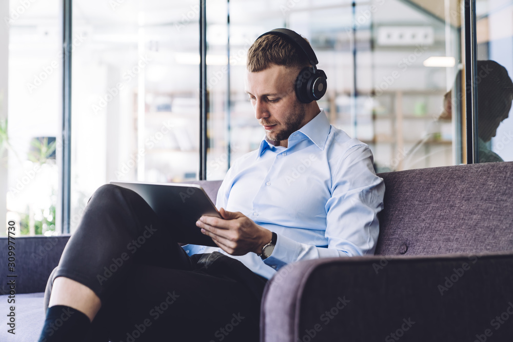 Wall mural Man with headphones sitting in office and using tablet