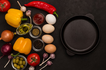 Frying pan, eggs and tomatoes, yellow and red peppers, garlic, spinach on a black background.
