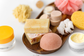 beauty, spa and wellness concept - close up of konjac sponge, crafted soap bars and body butter on wooden tray