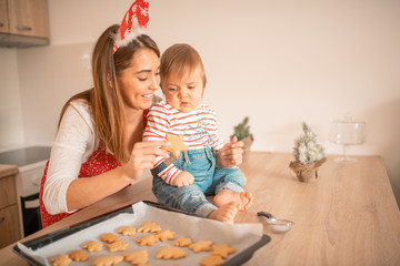 A mother holding her child and giving it a cookie in the kitchen.