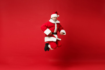 Smiling elderly gray-haired mustache bearded Santa man in Christmas hat posing isolated on red wall background. Happy New Year 2020 celebration holiday concept. Mock up copy space. Jumping having fun.