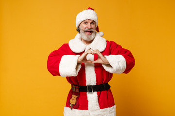 Fototapeta na wymiar Excited elderly gray-haired mustache bearded Santa man in Christmas hat posing isolated on yellow background. New Year 2020 celebration concept. Mock up copy space. Showing shape heart with hands.