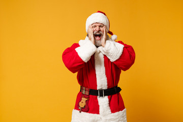 Fototapeta na wymiar Frustrated elderly gray-haired mustache bearded Santa man in Christmas hat posing isolated on yellow background. New Year 2020 celebration concept. Mock up copy space. Putting hands on cheeks scream.