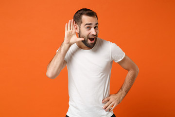 Curious young man in casual white t-shirt posing isolated on orange wall background studio...