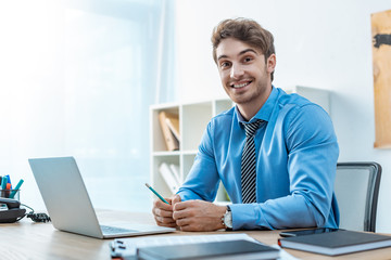 cheerful travel agent looking at camera while sitting at workplace