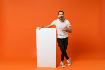 Cheerful young man in casual white t-shirt posing isolated on orange wall background in studio....