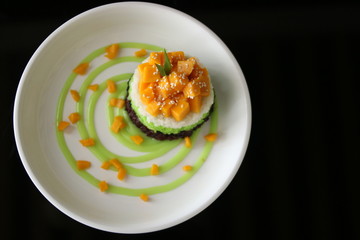 Delicious rice cake with manggo slice and sauce in black background