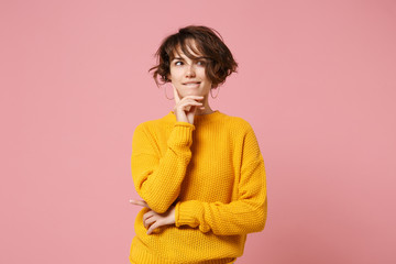 Pensive young brunette woman girl in yellow sweater posing isolated on pastel pink background,...