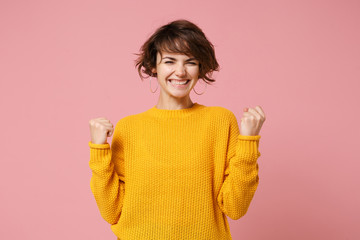 Joyful young brunette woman girl in yellow sweater posing isolated on pastel pink wall background studio portrait. People sincere emotions lifestyle concept. Mock up copy space. Doing winner gesture.
