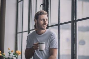 Inspired long-haired man having a cup of morning coffee.