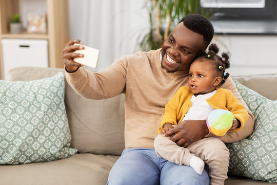 family, fatherhood and people concept - happy african american father with little baby daughter taking selfie by smartphone at home