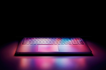 Half open laptop computer screen reflecting pastel colorful lights on the keyboard on black background