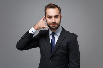 Handsome young business man in classic suit shirt tie posing isolated on grey background. Achievement career wealth business concept. Mock up copy space. Doing phone gesture like says call me back.