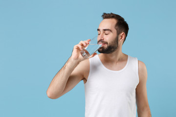 Bearded young man 20s years old perfect skin in white shirt hold water isolated on blue pastel wall...