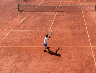 Child boy tennis player ready for service on a red - orange clay court. Top view, copy space. Training tournament match