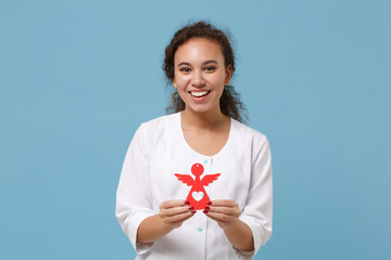 Smiling african american doctor woman isolated on blue background in studio. Female doctor in white medical gown hold red toy angel. Healthcare personnel medicine health concept. Mock up copy space.