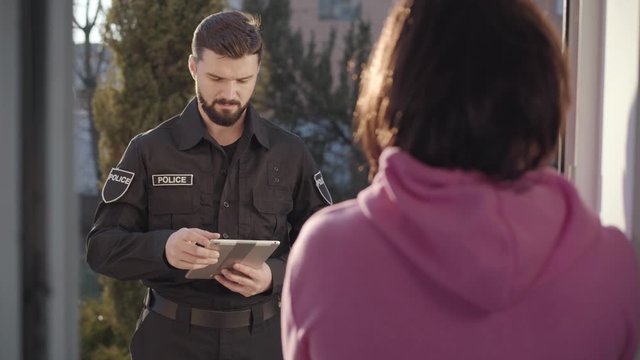 Back view of unrecognizable Caucasian brunette woman talking with police officer. Detective collecting witnesses about neighbor's robbery. Eyewitness, testimony, law enforcement.
