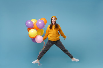 Crazy young woman girl in sweater and hat posing isolated on blue background. Birthday holiday party, people emotions concept. Mock up copy space. Celebrating holding colorful air balloons jumping.