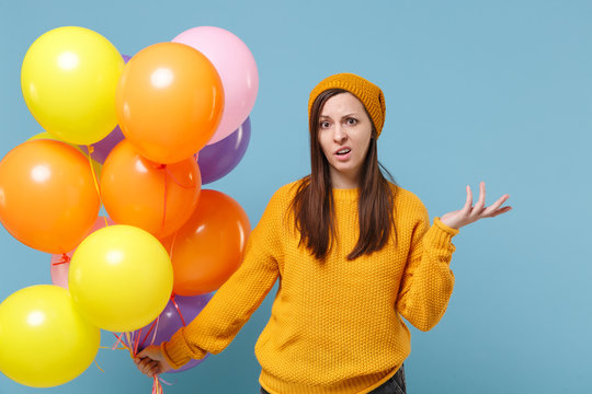 Perplexed young woman girl in sweater hat posing isolated on blue background. Birthday holiday party people emotion concept. Mock up copy space. Celebrating hold colorful air balloon spreading hands.