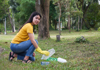Young woman in yellow t-shirt picking up litter in the park. Volunteering in park.