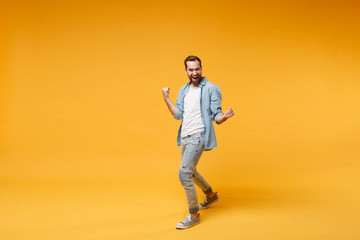 Fototapeta na wymiar Happy young bearded man in casual blue shirt posing isolated on yellow orange background studio portrait. People sincere emotions lifestyle concept. Mock up copy space. Clenching fists like winner.