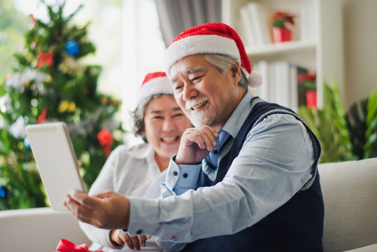 Senior Asian couple family celebration in Christmas day, Retired man and woman using tablet to video call with young family smile felling happy in living room at home. Merry Xmas and happy new year.