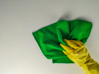 Top view of yellow rubber glove hand cleaning a white surface with green wipe rag as equipment for house domestic chores