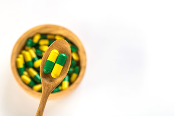 Capsule pills in wooden spoon and wooden bowl  on white background.