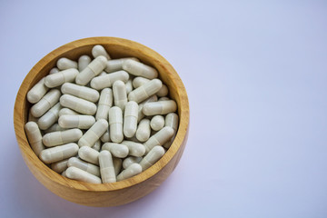 Capsule pills in wooden bowl  on white background.