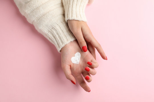 Woman hands, moisturizing cream for clean and soft skin in winter time, heart shape created from cream on pink background, space for text. Top view. Healthcare concept