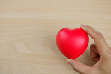 Red heart on hand on wooden background.